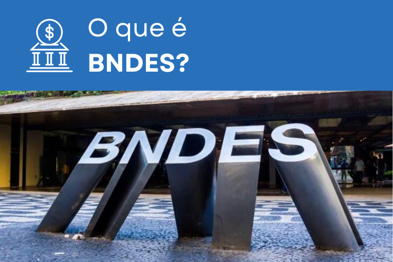 Essa imagem apresenta o texto: 'O que é BNDES' e mostra o logotipo do BNDES localizado na calçada em frente ao prédio da instituição no Rio de Janeiro. O logotipo é composto pelas letras 'BNDES' esculpidas em metal na calçada.